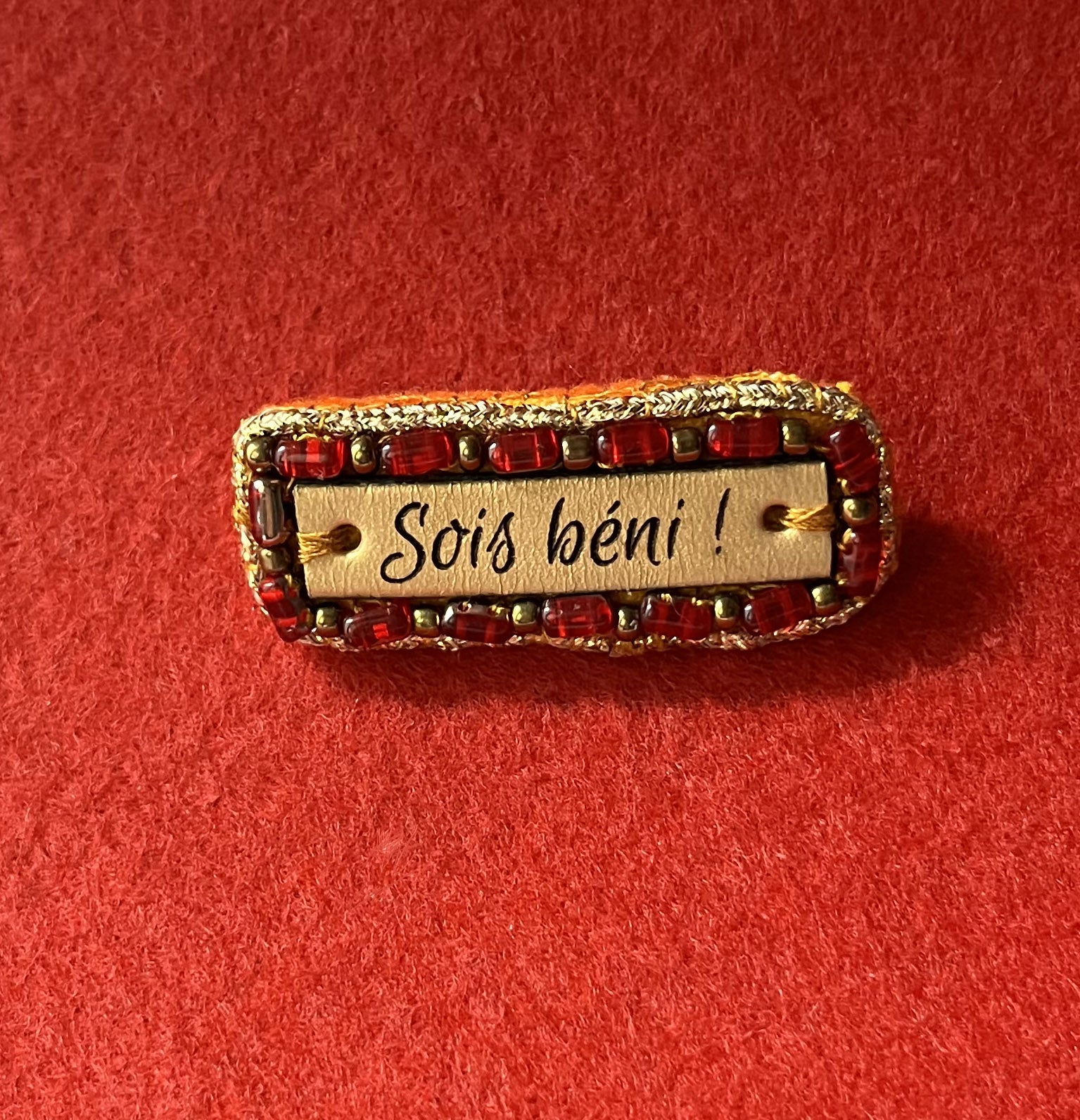 Broche à message en cuir gravé "sois béni" en perles rouges et dorées